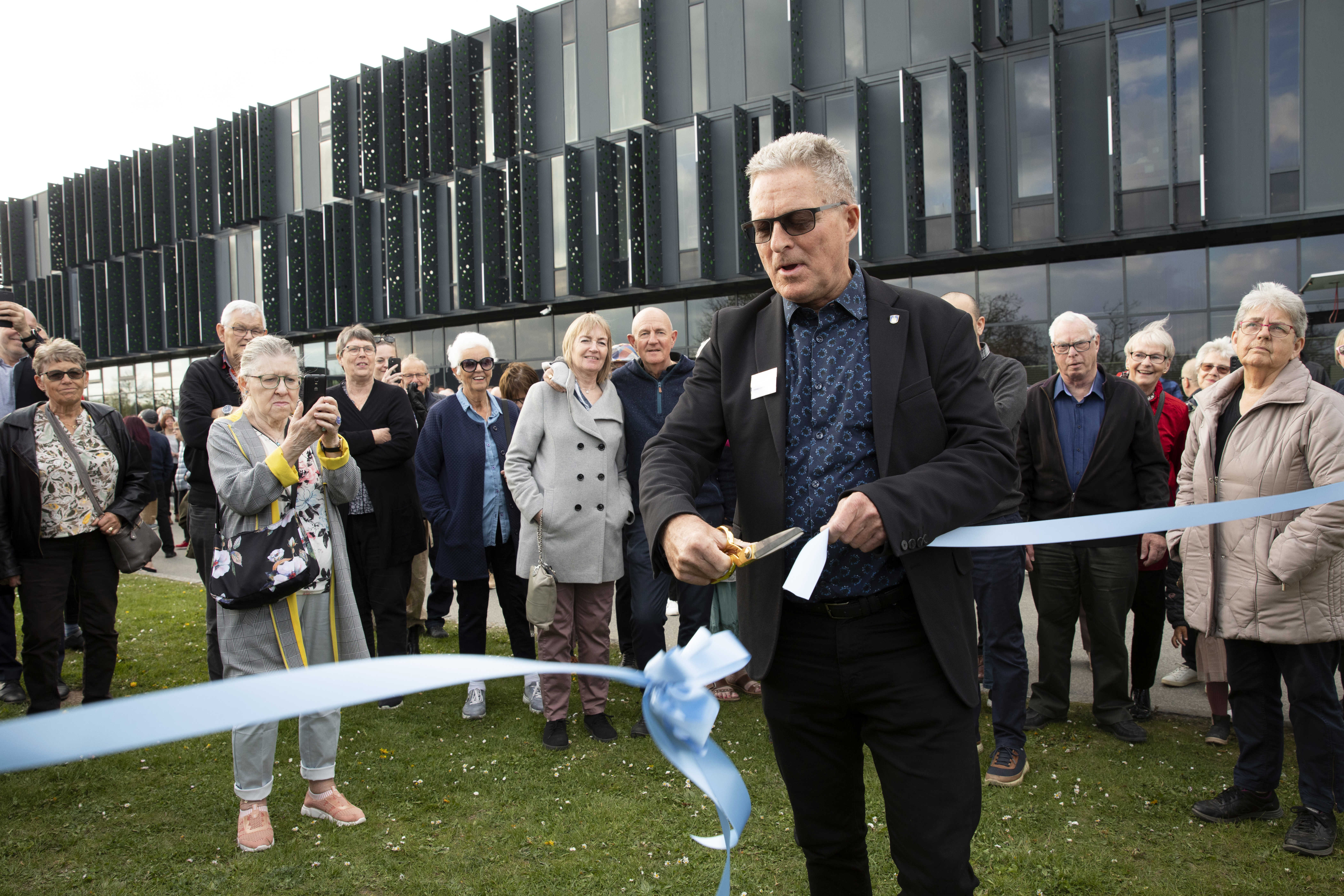 Forhenværende borgmester Kent Magelund klipper et lyseblåt satinbånd med en guldsaks ifm. indvielse af udstillingen af de tre forslag til udviklingsplanen, i baggrunden står en gruppe borgere.